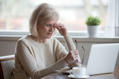 woman rubbing eye in white sweater