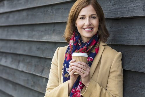 woman tan jacket and floral scarf holding a cup of coffee